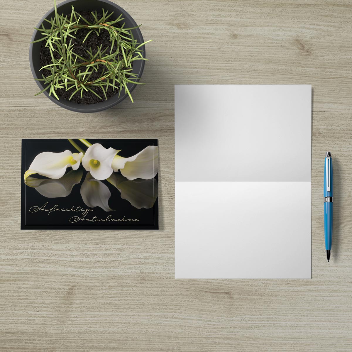 Hochwertige nachhaltige Trauerkarte mit weißer Blüte und elegantem Design neben weißem Kuvert und Stift auf Holztisch.